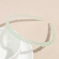 Gros plan d'un serre-tête vert clair perlé avec une texture en résine sur fond beige - Vert Perle de Rêve