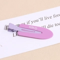 Close-up of pink and purple matte duckbill hair clip with Grape text on a beige surface - Letter Purple