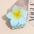 Detail view of a translucent blue plumeria hair claw clip on a stylish Vogue magazine background - Blue