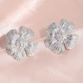 Primer plano de aretes de flores plateadas con textura de cinco pétalos sobre seda rosa - Flor Plateada
