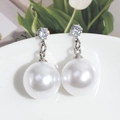 Detalle macro de elegantes pendientes de perla con perno plateado sobre cerámica - Perla Blanca y Estrás
