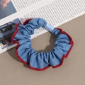 Scrunchie in denim blu con bordi pieghettati rossi e fibbia azzurra su sfondo di rivista - Azzurro