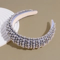 Detalle de una diadema gruesa con perlas grises sobre un soporte decorativo blanco - Gris