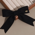 Détail d'un nœud en tricot noir avec plaque dorée gravée LOVE sur un plateau à bijoux - Noir