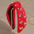 Dettaglio di fascia rossa annodata con strass, ciondoli a cuore e scritta LOVE su supporto - Cuore in Strass Rosa
