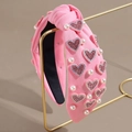 Dettaglio di cerchietto rosa annodato con paillettes a cuore e perle su un supporto - Perla Pieno Cuore Rosa