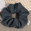 Close-up of a dark grey wool scrunchie with Happiness label on a rustic magazine background - Dark Gray