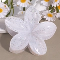 Detail view of the white glitter floral hair claw clip on a warm beige background - Lily White