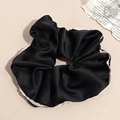 Detail of a black satin scrunchie with white lace trim on a soft beige background - Black