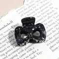 Macro shot of a black and white speckled triangular claw clip on a vintage magazine page - Bow / Glossy Black (Splash Ink)