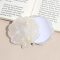 Close-up of shell-shaped makeup mirror with pearl white finish and gold line detailing - White