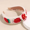 Nahaufnahme eines weiß gestrickten Stirnbands mit Erdbeermuster und weichen Endstücken - Rote Erdbeere mit grünem Stiel