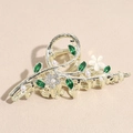 Large golden hair claw clip with green enamel leaves, crystals, and pearls on a beige surface - Floral Claw Clip / Gold