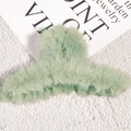 Detailed view of mint green plush faux fur hair claw clip against a white textured wall - Green