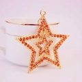 Golden double star keychain pendant with amber rhinestones leaning on a white cup - Orange Yellow
