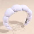 Detail showing the white fluffy sponge headband with soft terry cloth texture on a display stand - White