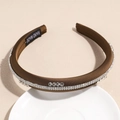 Détail du bandeau en satin marron avec double rangée de strass sur une assiette blanche - Brun Foncé