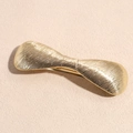 Macro detail of golden metal bow hair clip with textured vertical brushed finish - Ribbon Bow Gold