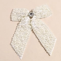 Detailed macro view of white faux pearls and central oval rhinestone on a bow hair clip - Off White