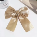 Detailed top view of large champagne gold satin bow hair clip on a minimalist white surface - Camel