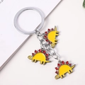 Cartoon Stegosaurus Schlüsselanhänger mit drei gelb-roten Metallanhängern an einem Ring - Gelber Stegosaurus