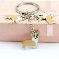 Dettaglio di tre ciondoli Corgi in metallo su un portachiavi sopra una scatola regalo - Stile Trio Corgi Giallo