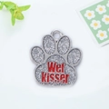 Macro shot of silver paw-shaped pet tag with glitter texture and red Wet Kisser lettering - Silver