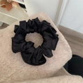 Detail shot of a black satin scrunchie with pleated edges on a soft beige fabric - Black