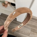 Détail d'un serre-tête en velours marron clair torsadé avec un emblème H en métal argenté - Beige