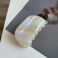 Gros plan d'une grande pince à cheveux blanc nacré avec lettrage doré de marque - 8cm x 4cm