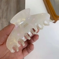 Detailed view of pearlescent white acetate shark hair claw clip with golden branding text - White Enamel
