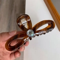 Close-up of a tortoiseshell bow hair claw clip with a sparkling center gemstone detail - Caramel color