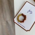 Détail macro d'une bague élastique en bois brun et perles de résine ambre sur carte - Jaune Vert+Marron Patchwork