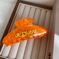 Detalle de pinza para el pelo naranja de acetato con letras Je t'aime amarillas 3D - Concha Naranja