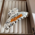 Detalle de pinza para pelo jaspeada con letras naranjas JE T'AIME sobre terciopelo blanco - Marble