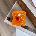 Detail of a cartoon orange monster hair claw clip with a single eye and red tongue detail - Orange One-Eyed Monster