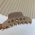 Detail of cream acetate hair claw clip featuring stylish metallic eyelet decorations - Beige