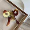Detail of a medium acetate bow hair claw clip with tortoise pattern on a beige tray - Milk Coffee