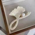 Detailaufnahme einer Ginkgoblatt-Haarklammer mit Perle auf einer hellen Schmuckschatulle - Creme Marmor