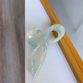 Detail view of the elegant marble blue acetate bow hair claw clip against a wooden frame - Blue Patterned