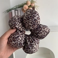 Dettaglio di un elastico per capelli in velluto leopardato tenuto in mano in casa - Caffè Chiaro