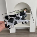 Dettaglio di una molletta per capelli a forma di mucca con stampa bianca e nera in mano - Pinza per capelli a forma di mucca / 10.5cm x 5cm / Stampa Mucca Bianca e Nera