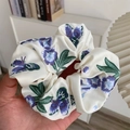 Nahaufnahme eines beigen Seiden-Scrunchies mit eleganter Blumenstickerei und weicher Textur - Weiß Blau Blumig Bestickt