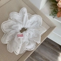 Dettaglio ravvicinato di uno scrunchie in pizzo bianco con perle e etichetta di marca - Bianco puro