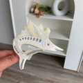 Dettaglio macro di un fermaglio per capelli in acetato a forma di pesce con trama perlata - Beige