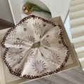 Detail eines cremefarbenen Oversize-Haargummis mit Sonnenmuster und dunkler Naht - Beige