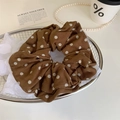 Nahaufnahme eines braunen Cord-Haargummis mit weißen Punkten in einem Metallkorb - Karamell Punktmuster Scrunchie