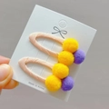 Close-up of colorful pom pom hair clips on pink fabric base with soft fuzzy texture - Gold Yellow