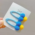 Detailed view of pom-pom hair clips on a card featuring blue and yellow plush balls - Lake Blue
