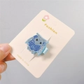 Detailed macro view of an owl hair clip with blue and silver rhinestones on card - Blue Owl Style